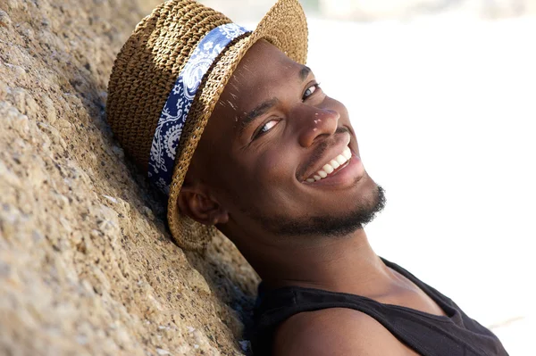 Giovane uomo sorridente con cappello rilassante all'aperto — Foto Stock