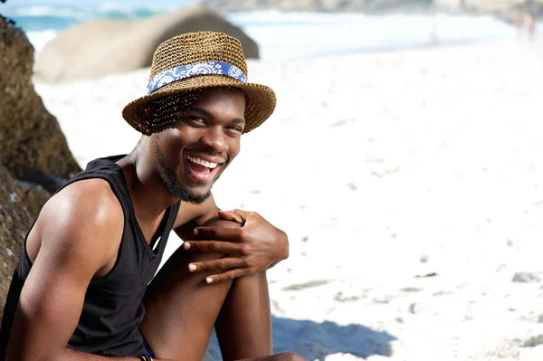 Mutlu adam şapka ile plajda otururken — Stok fotoğraf
