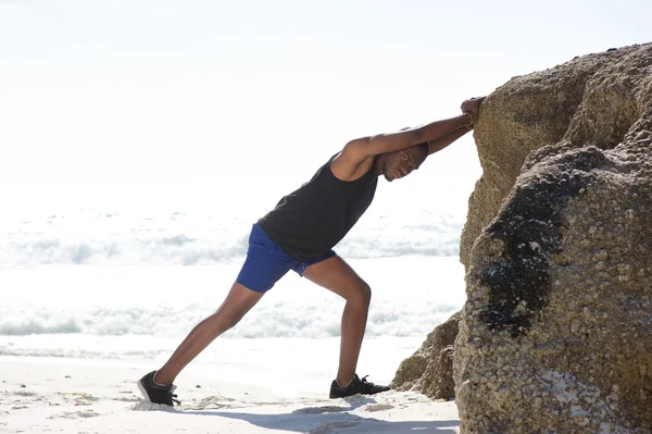 Esporte homem empurrando na rocha na praia — Fotografia de Stock