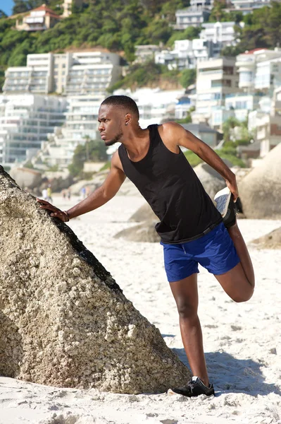 Schöner junger Sportler dehnt sich am Strand aus — Stockfoto