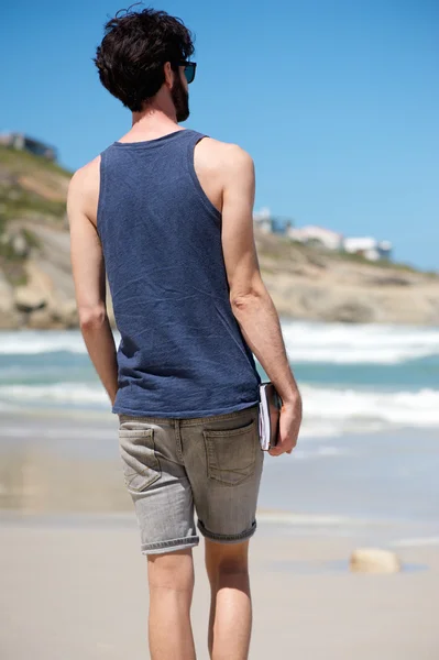 Man on vacation walking alone on beach with book — Stock Photo, Image