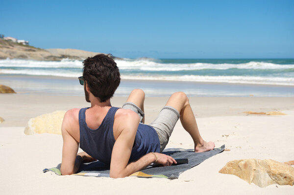 Молодой человек сидит один на уединенном пляже
