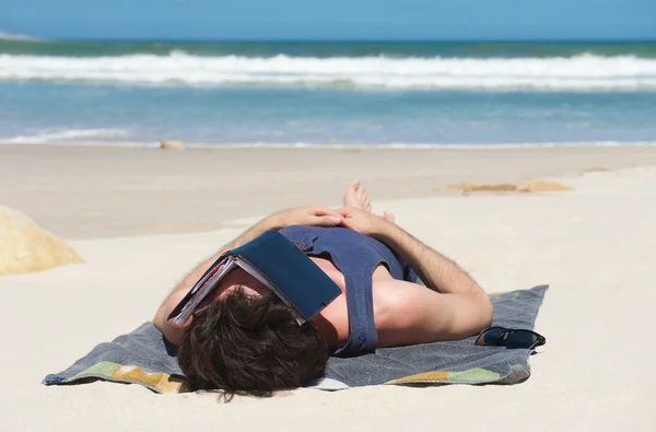 Man slapen op afgelegen strand met boek die betrekking hebben op gezicht — Stockfoto