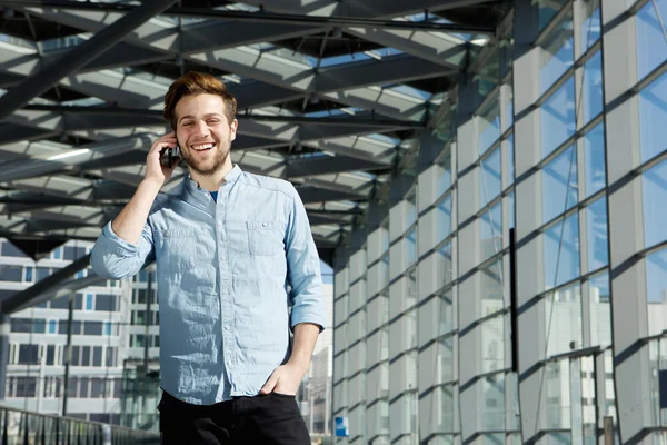Молодой человек улыбается внутри здания с мобильным телефоном — стоковое фото