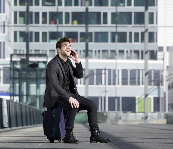 Homem de viagem feliz falando no telefone celular enquanto sentado na mala — Fotografia de Stock