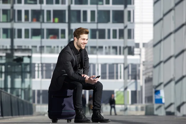 Glad ung man väntar vid station med mobiltelefon — Stockfoto