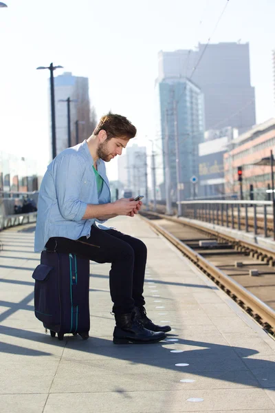 Jonge man zittend op de trein station platform SMS-berichten — Stockfoto