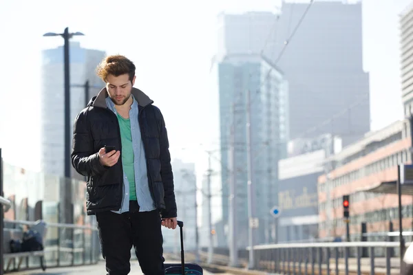 Mladý muž s vakem a mobilní telefon ve městě — Stock fotografie