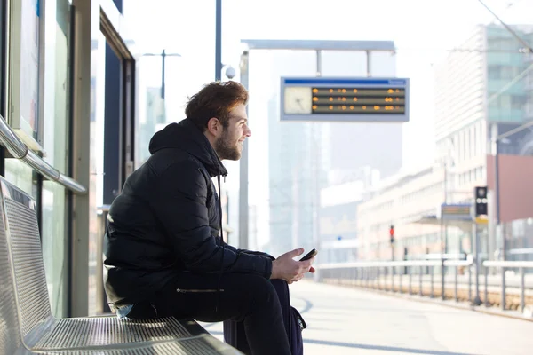 Lachende jonge man zittend op de Bank op treinstation — Stockfoto