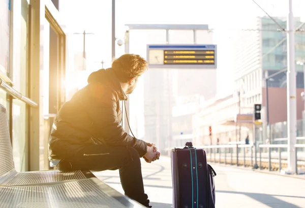 Giovane seduto alla stazione ferroviaria guardando l'orario — Foto Stock