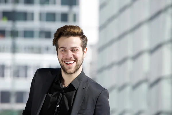 Aantrekkelijke jonge man met baard glimlachend in de stad — Stockfoto