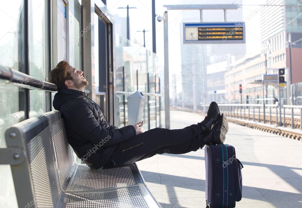 Smiling young man sitting with bag waiting for train