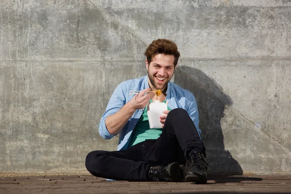 Jovem feliz comendo comida asiática com pauzinhos — Fotografia de Stock