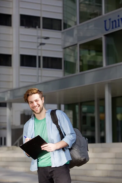 Estudante universitário sorrindo de pé fora com bloco de notas — Fotografia de Stock