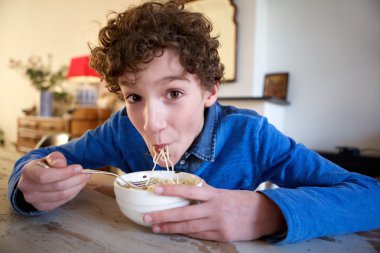 Happy boy eating noodles at home clipart