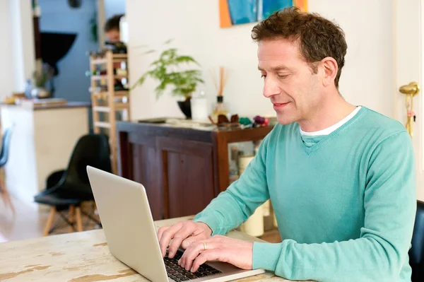 Volwassen mannelijke volwassene zitten aan tafel thuis met behulp van laptop — Stockfoto