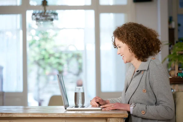 Mulher mais velha sorrindo e usando laptop em casa — Fotografia de Stock