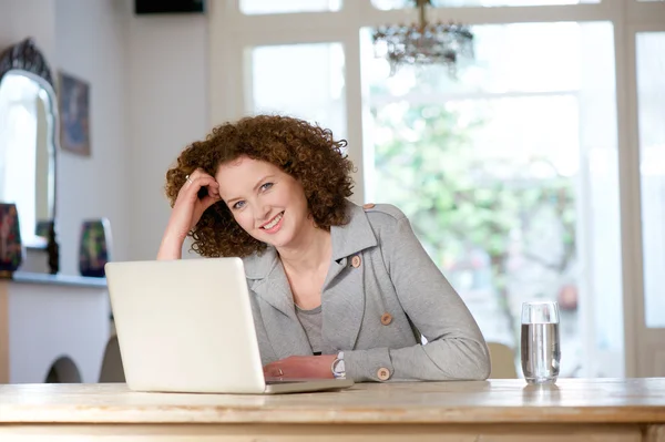 Leende äldre kvinna sitter vid bord med laptop — Stockfoto