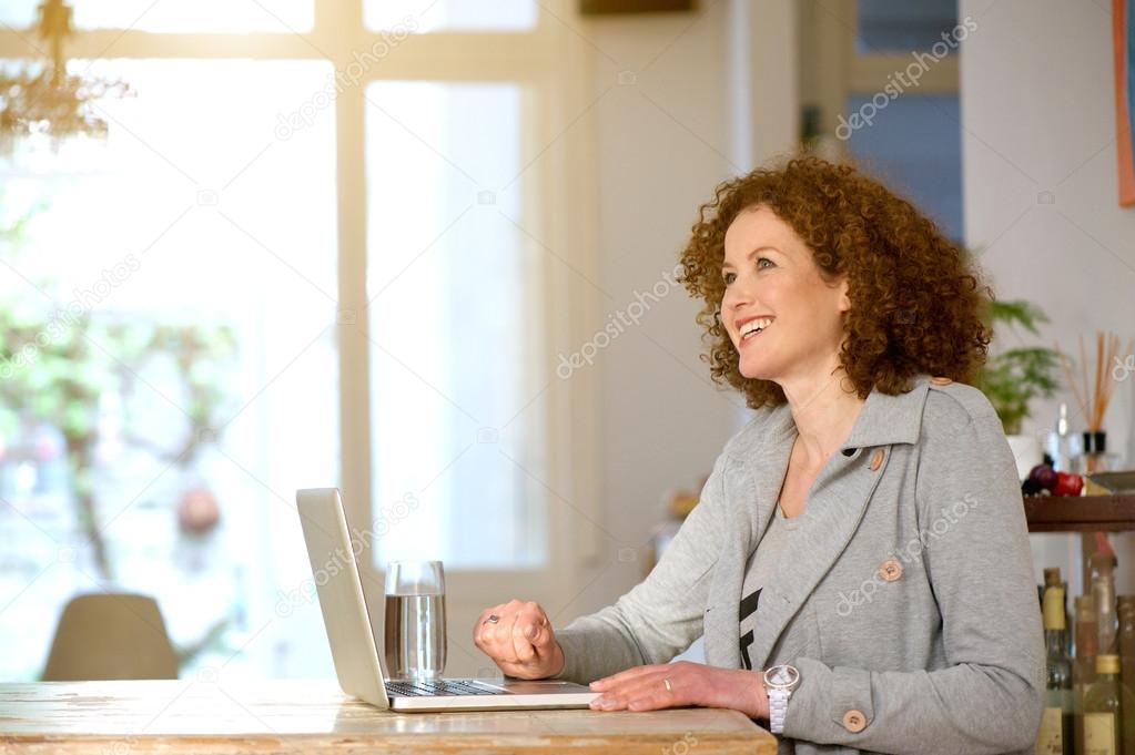 Happy middle aged woman using laptop at home