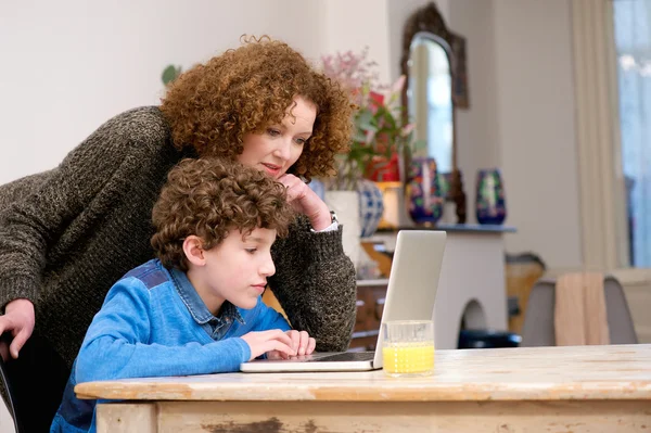 Mujer ayudando a niño pequeño usando la computadora en casa — Foto de Stock