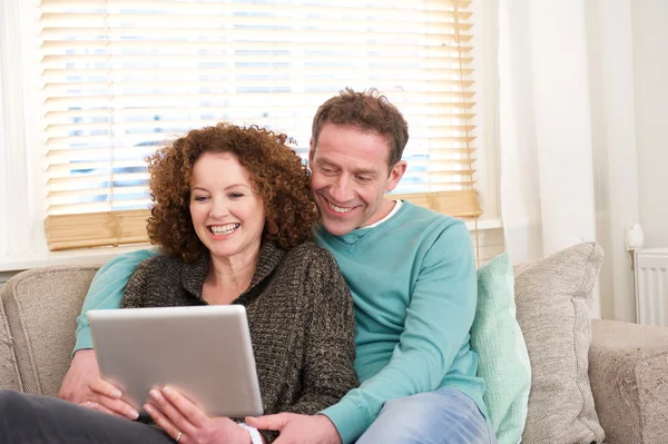 Happy couple sitting on sofa at home looking at computer tablet — Stock Photo, Image