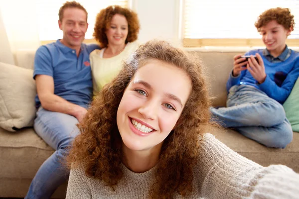 Szczęśliwa młoda dziewczyna przy selfie z rodzicami w tle — Zdjęcie stockowe