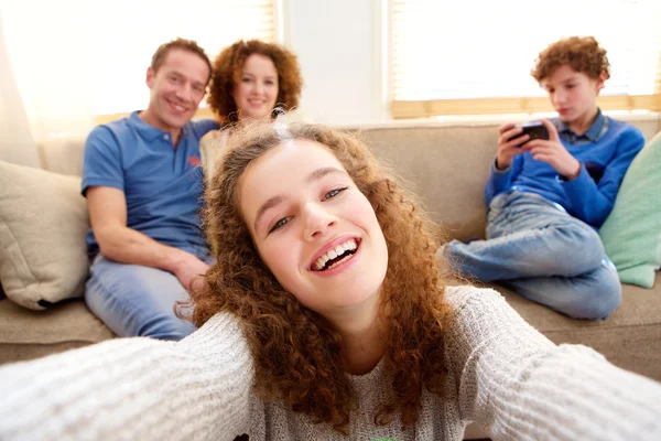 Chica feliz tomando una selfie con la familia en el fondo — Foto de Stock