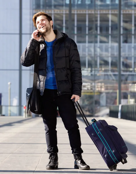Smiling man at station with bag talking on mobile phone — Stock Photo, Image