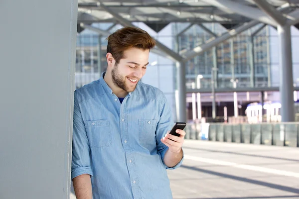 Улыбающийся молодой человек смотрит на мобильный телефон — стоковое фото