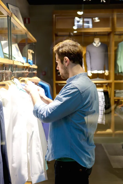 Young man selecting shirts to buy at shop — Stock Photo, Image