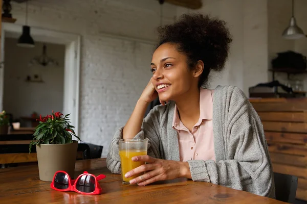Mujer joven sonriente sentada en casa con un vaso de jugo de naranja — Foto de Stock