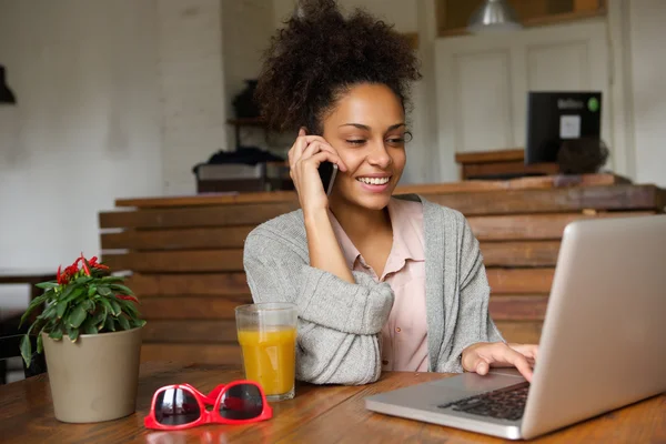 Mujer joven sonriente usando el ordenador portátil y hablando por teléfono móvil —  Fotos de Stock