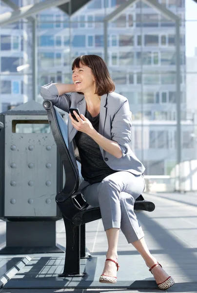 Mujer alegre de negocios sentada en la ciudad con teléfono móvil —  Fotos de Stock
