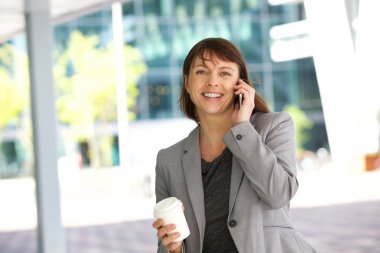 yürüyüş ve cep telefonuyla konuşurken gülümseyen iş kadını