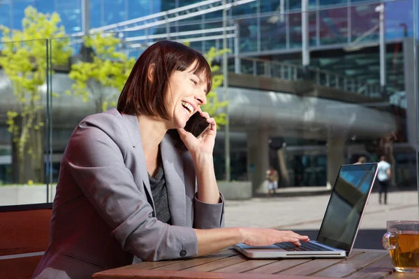 Mujer de negocios feliz hablando en el teléfono móvil y trabajando en el ordenador portátil —  Fotos de Stock