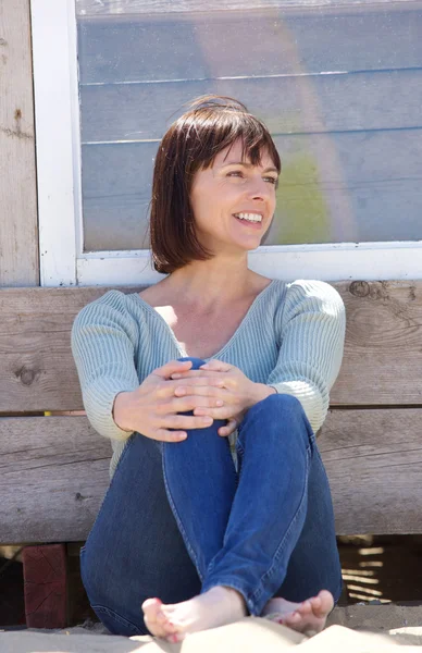 Happy middle aged woman in jeans sitting outside — Zdjęcie stockowe