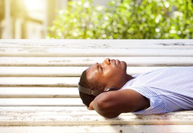 Bir bankta kulaklık ile yatan genç siyah adam