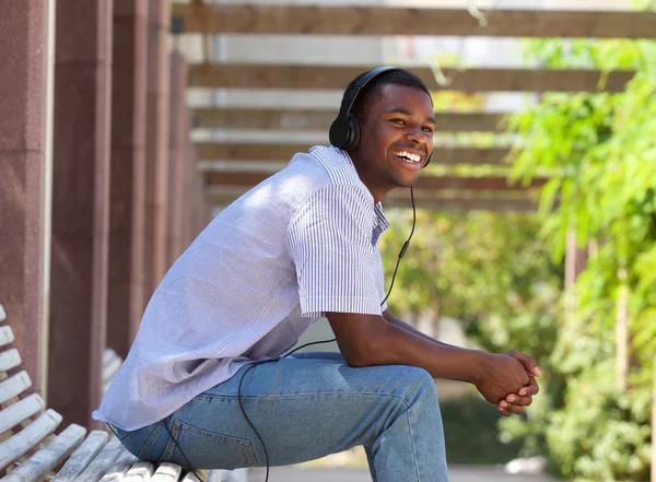 Chico feliz sentado en la rama del parque con auriculares —  Fotos de Stock