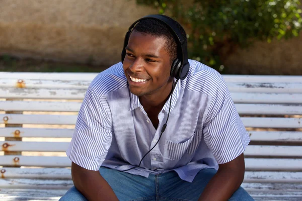 Χαμογελαστός νεαρός άνδρας κάθεται στο παγκάκι με ακουστικά — Φωτογραφία Αρχείου