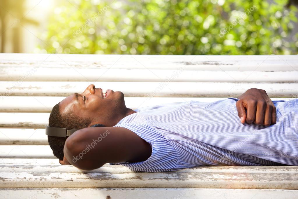 Happy young man lying on park bench with headphones