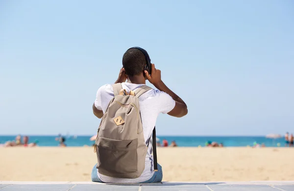Homem sentado na praia com saco e fones de ouvido — Fotografia de Stock