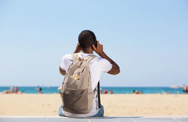 Man sitter på stranden med väska och hörlurar — Stockfoto