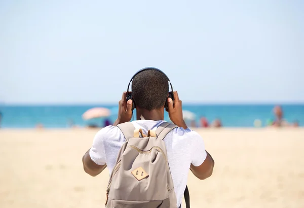 Junger Mann mit Kopfhörer und Tasche steht am Strand — Stockfoto