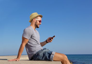 Cep telefonu ile deniz kenarında oturan mutlu genç adam