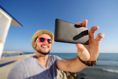Genç adam tatilde plajda selfie alarak gülümseyerek.