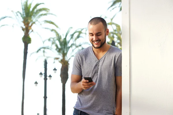 Glimlachend jonge man die leest sms-bericht op mobiele telefoon — Stockfoto