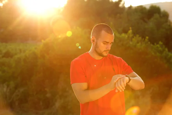 Runner standing outside looking at watch — Stock Photo, Image