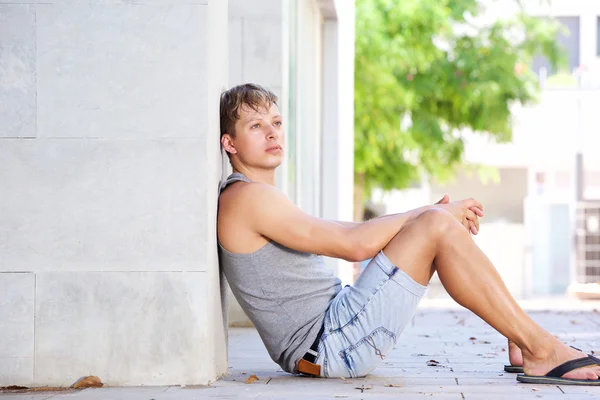 Νεαρός άνδρας κάθεται στο πάτωμα εκτός ψάχνει μακριά σκέψης — Φωτογραφία Αρχείου