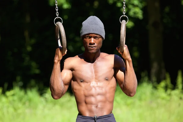 Musculoso afroamericano hombre sosteniendo anillos de gimnasio — Foto de Stock
