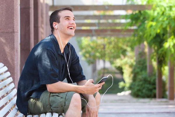 Sorrindo homem sentado fora com telefone celular e fones de ouvido — Fotografia de Stock